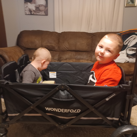 Two young boys sitting comfortably in a Wonderfold wagon indoors, enjoying playtime together