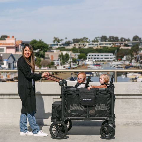 Woman strolling with two kids in the W2 Luxe Pro 2-seater wagon, showcasing its all-terrain wheels and spacious design
