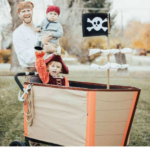 Family dressed as pirates poses beside their WonderFold wagon decorated as a pirate ship, complete with a flag featuring a skull and crossbones