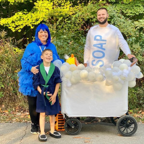 Family dressed in creative bubble bath-themed costumes poses with their WonderFold wagon transformed into a bathtub filled with balloons representing bubbles
