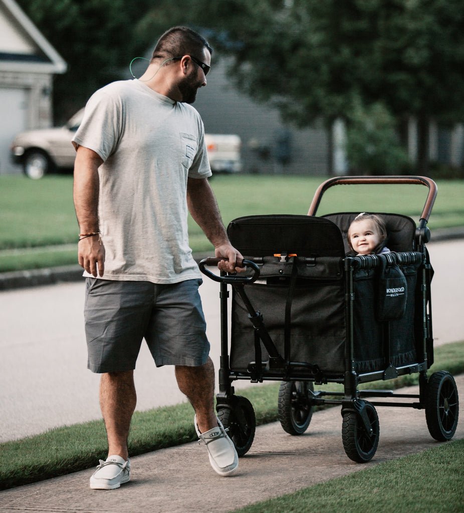 Father pulling a smiling child in a WonderFold stroller wagon using the optional pull handle