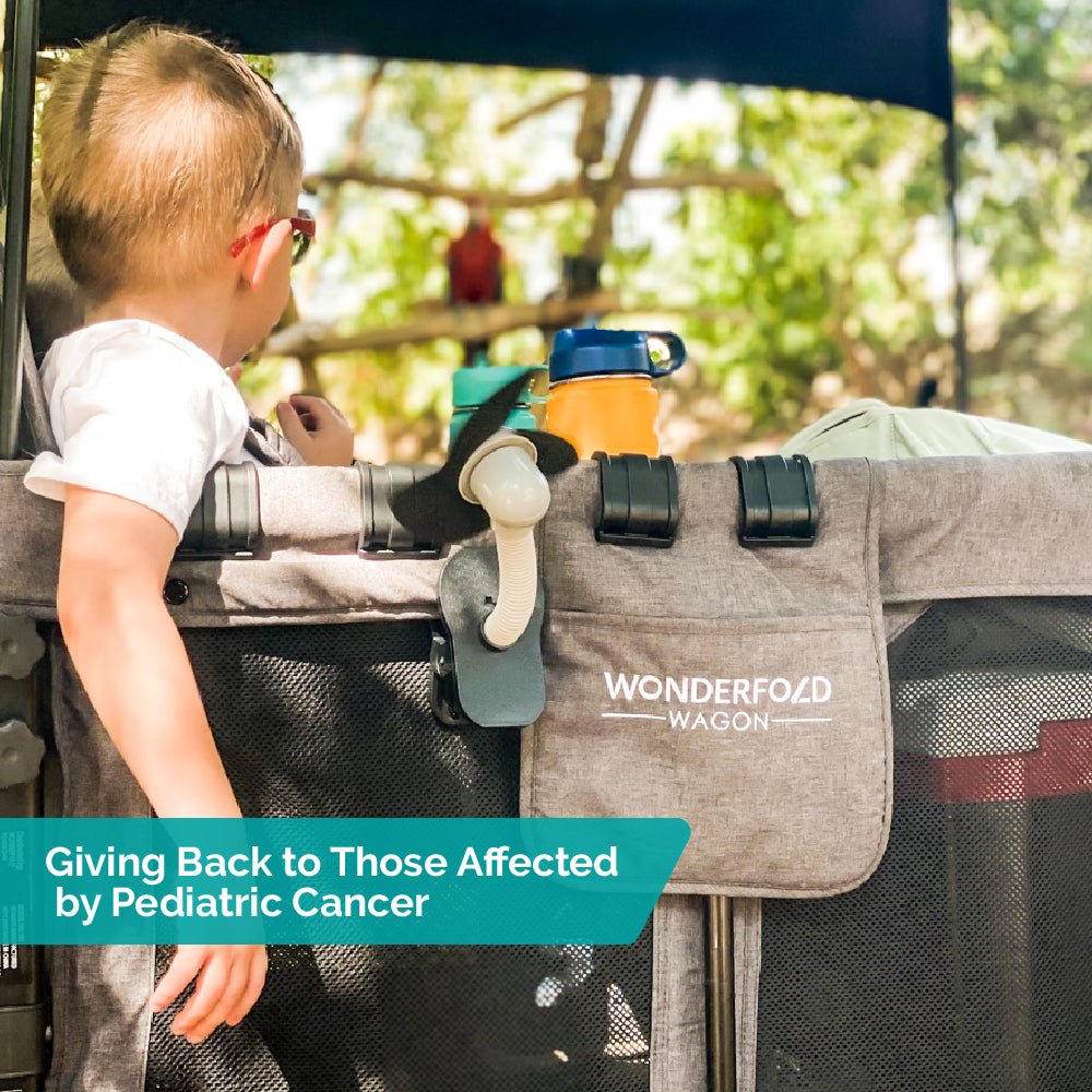 Child sitting in a WonderFold wagon with a tag reading “Giving Back to Those Affected by Pediatric Cancer.”