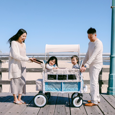 A couple walking along a boardwalk near the beach, happily pushing two children in a Volkswagen WonderFold wagon
