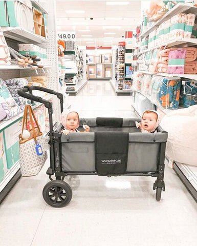 Two toddlers seated in a WonderFold W1 stroller wagon during a shopping trip at a store